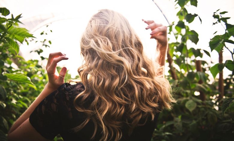 blonde woman showing her natural hair growth while she stands in a garden